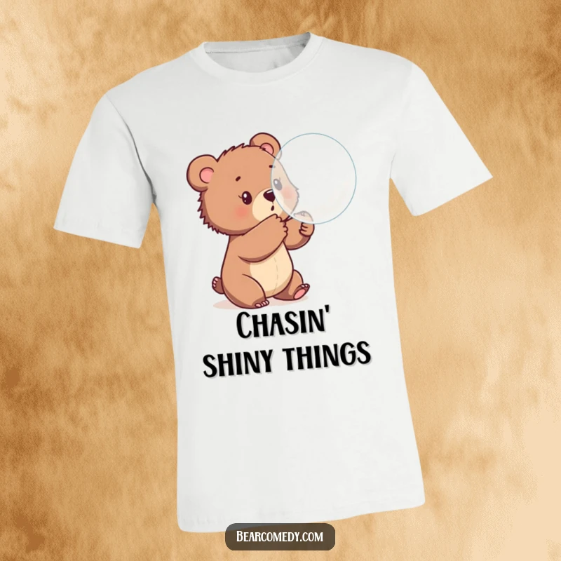 Funny t-shirt with a curious bear cub playfully swatting at a large, shiny, bouncing bubble, symbolizing joy and innocent amusement.